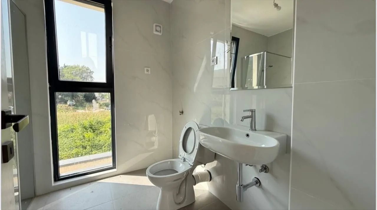 Modernly equipped bathroom with a washbasin, toilet, and a large window.