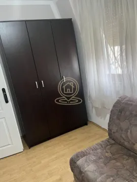Manja spavaća soba sa tamnim drvenim ormanom i foteljom pored prozora. - image 4
