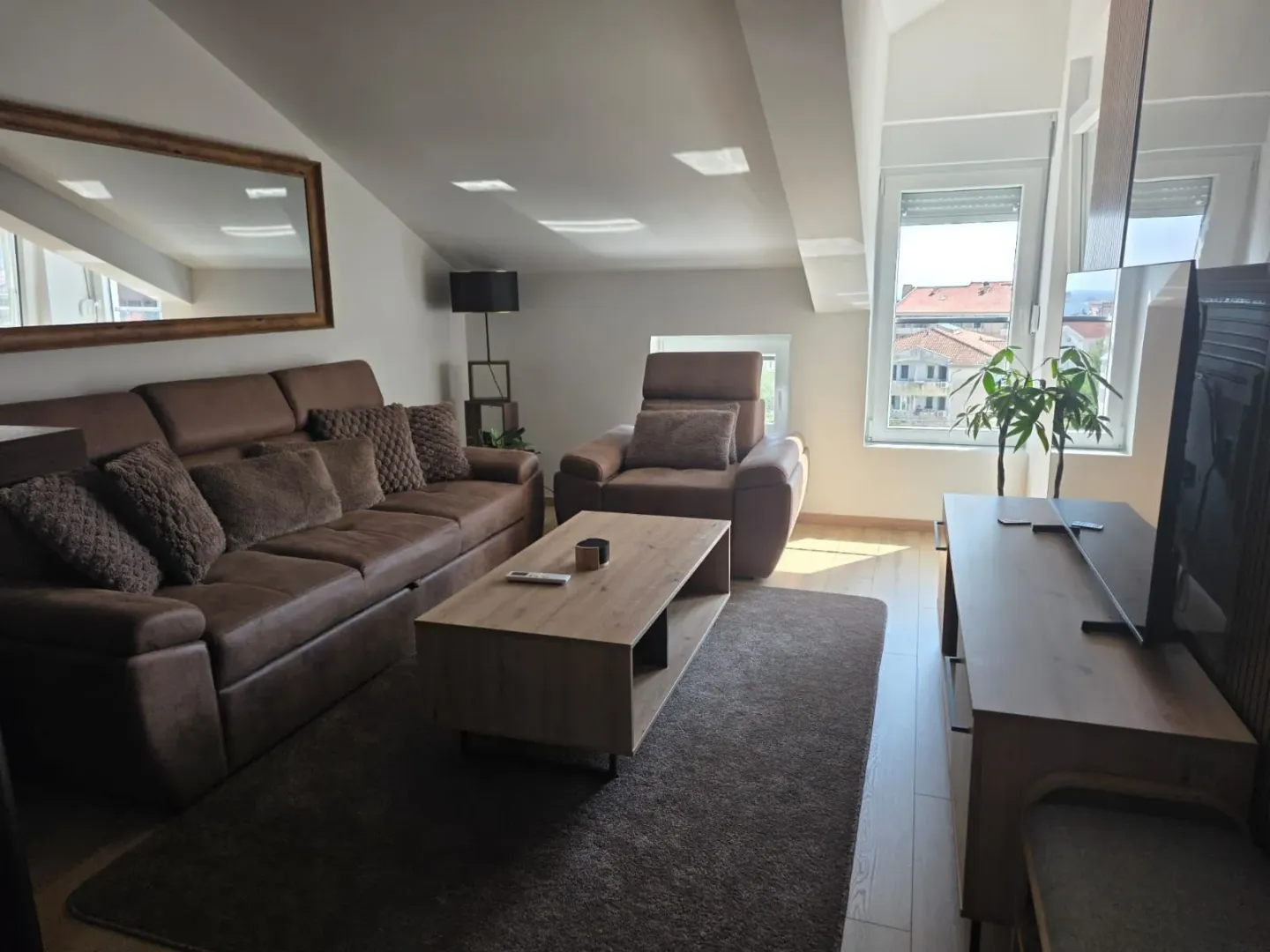 Living room with a brown sofa set, wooden coffee table, and television under a sloped ceiling.