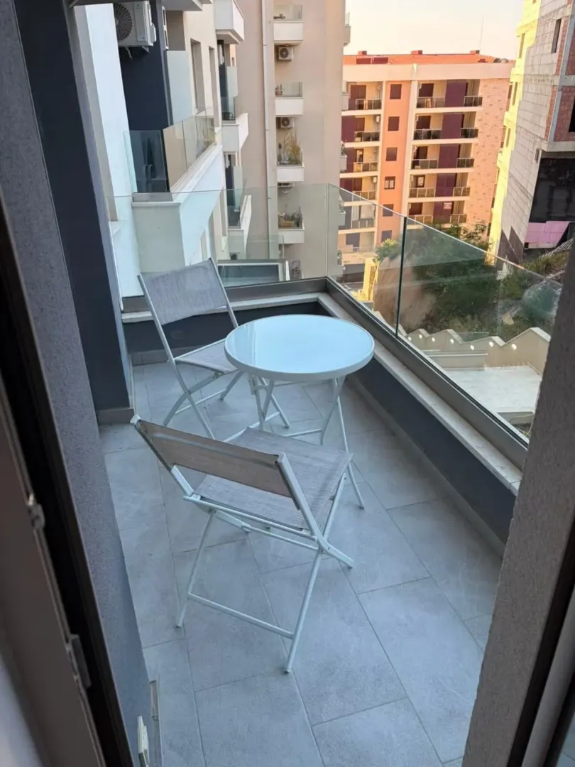 Small furnished balcony with glass railing and neighborhood view.