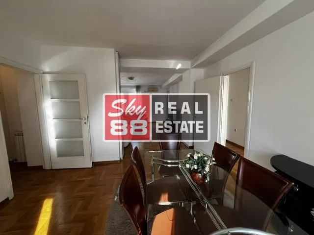 Trpezarija sa staklenim stolom i tamnim drvenim stolicama u stanu.