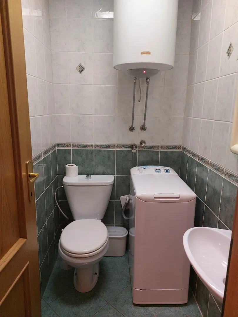 A small bathroom with a toilet, washing machine, and water heater.