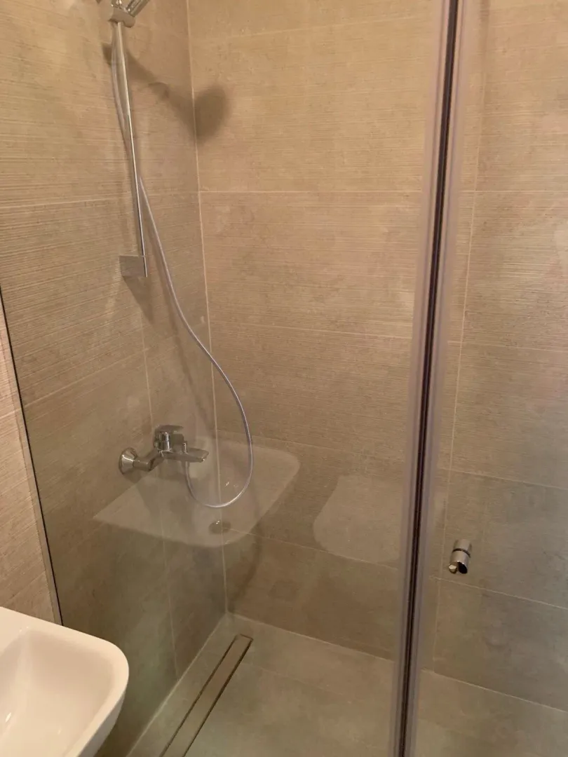 Walk-in shower with glass partition and beige ceramic tiles.