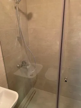 Walk-in shower with glass partition and beige ceramic tiles. - image 8
