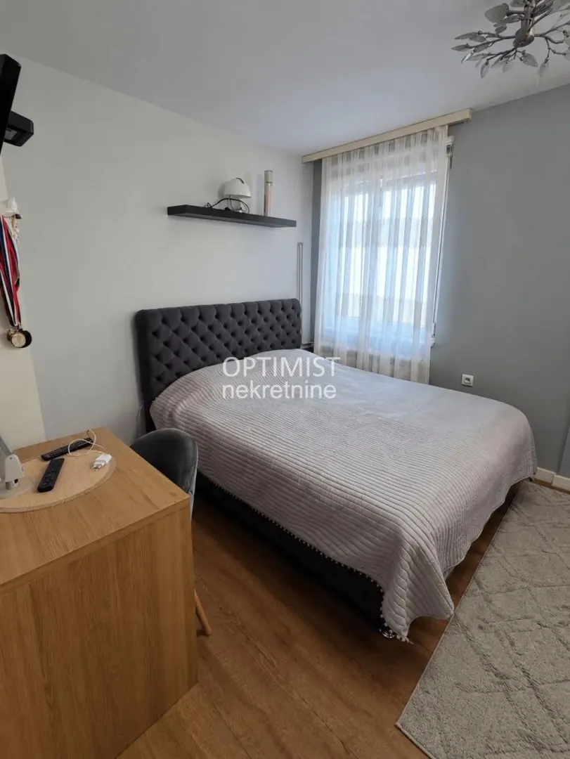 Nameštena spavaća soba sa bračnim krevetom, radnim stolom i prozorom.
