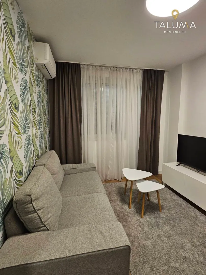 Living room with a grey sofa, television, and botanical wallpaper.