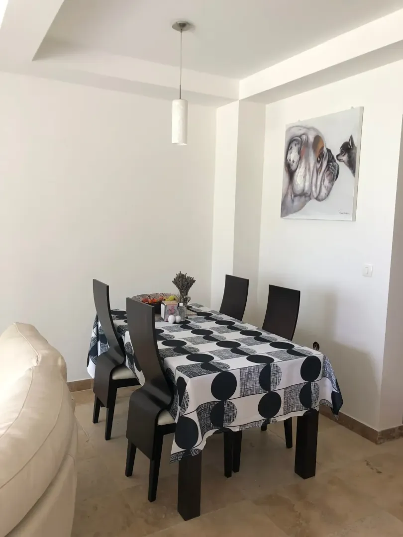 A dining table with a black and white patterned tablecloth and a dog painting on the wall.