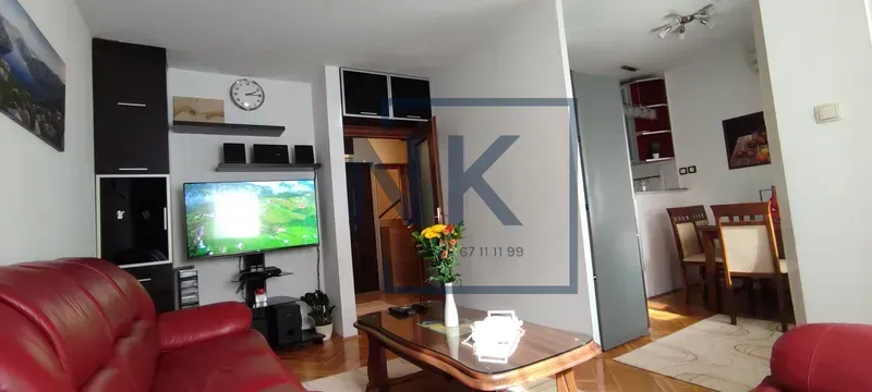 Dnevna soba sa crvenom kožnom garniturom, televizorom i pogledom prema trpezariji.