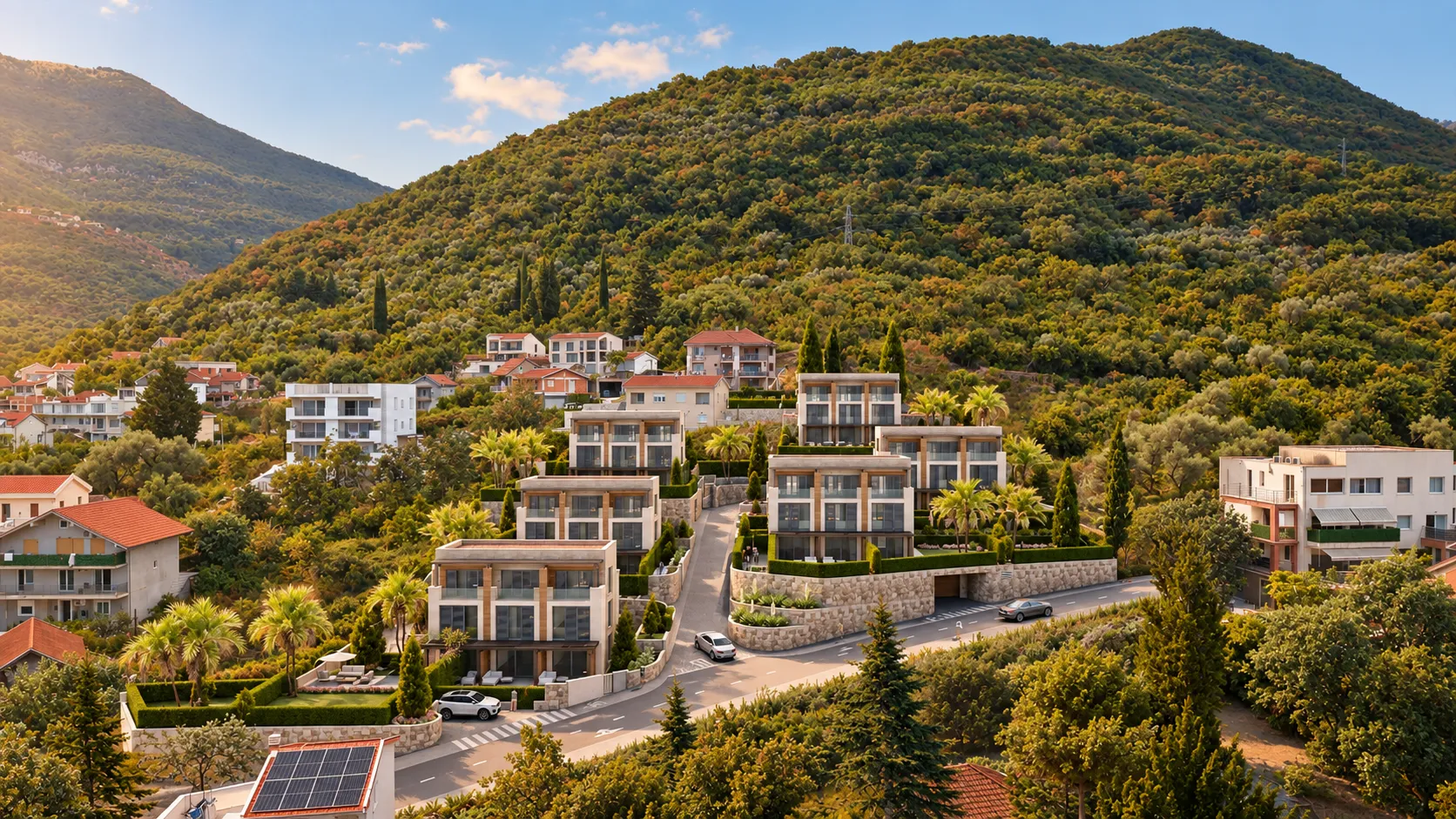 Pogled sa visine na moderno stambeno naselje okruženo zelenilom i brdima.