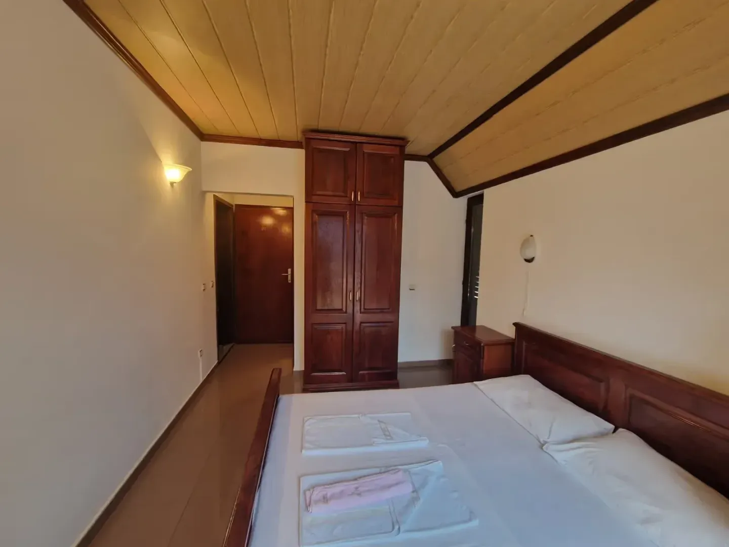Bedroom with a double bed, wooden wardrobe, and wood-paneled ceiling.