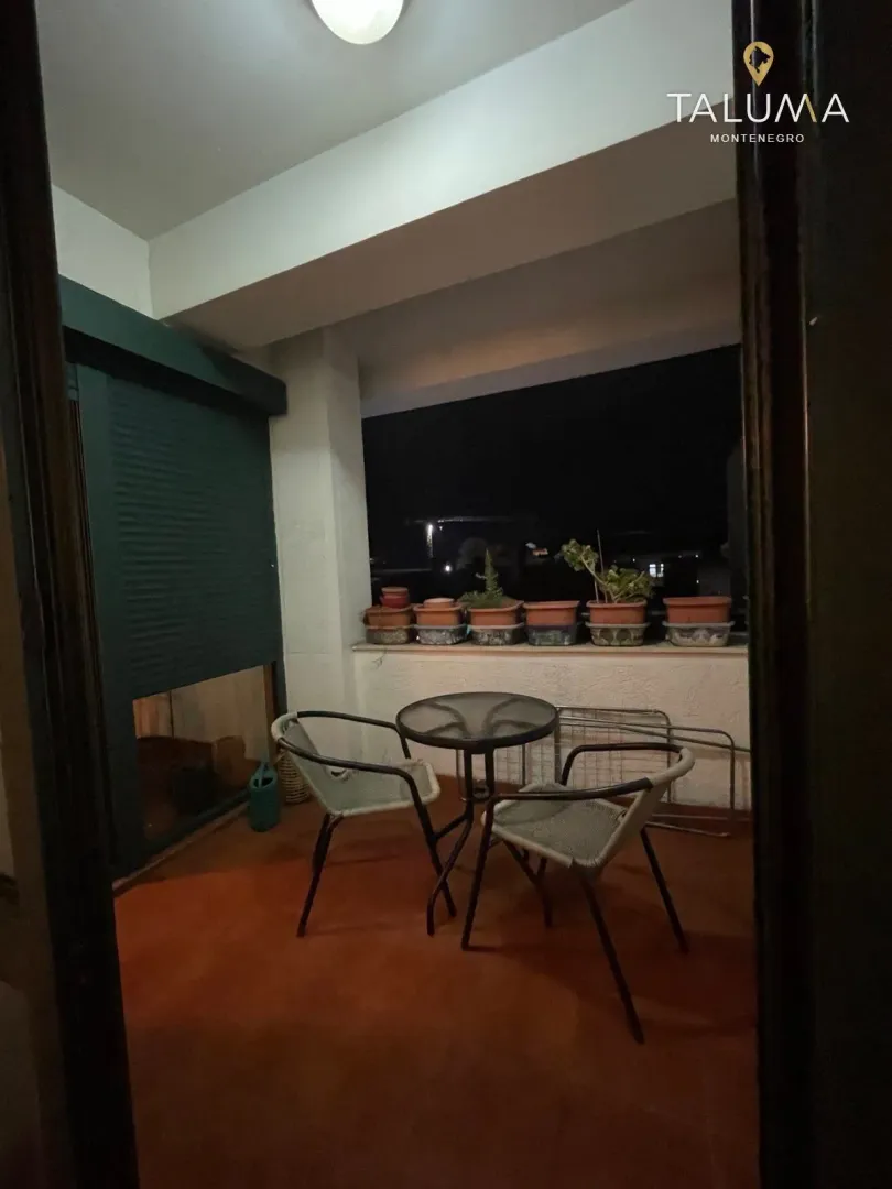 Natkrivena terasa sa stolom, stolicama i saksijama sa cijećem noću.