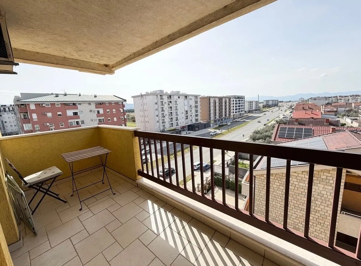 Smaller covered balcony with seating furniture and a view of the city street and buildings.