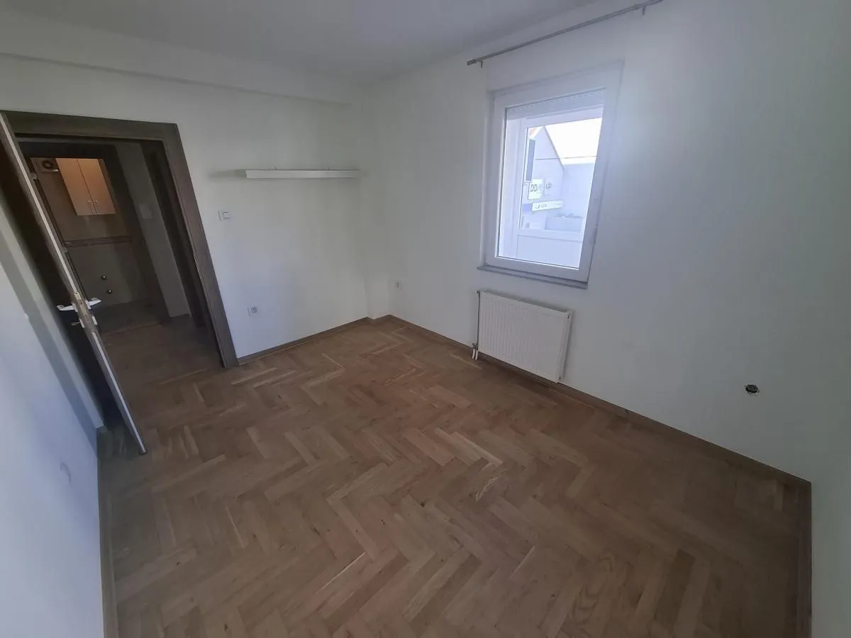 Prazna soba sa parketom i prozorom.