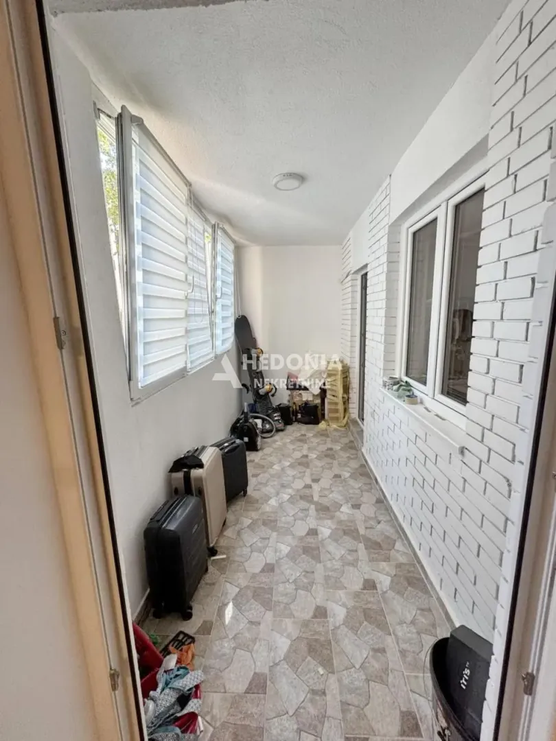Zastakljeni balkon sa pločicama na podu i odloženim stvarima.