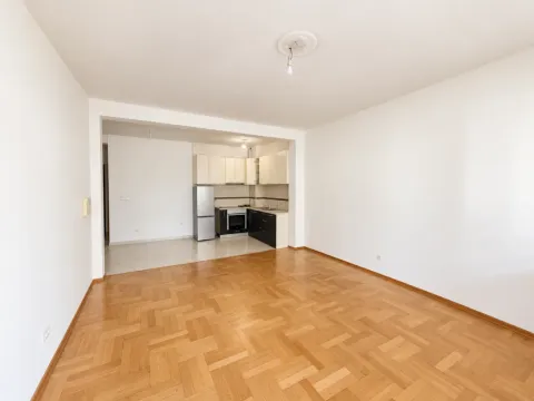 Prazna dnevna soba sa parketom i pogledom na kuhinju u pozadini. - image 2