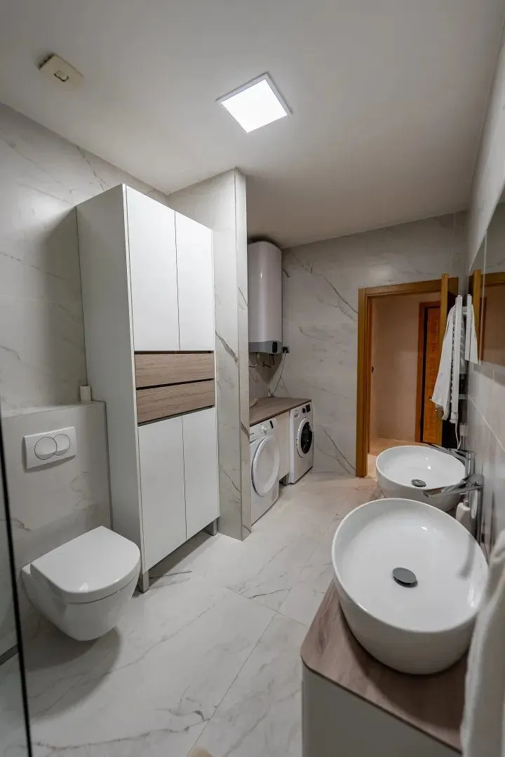 Modern bathroom with two washbasins, toilet bowl, and washing machines.