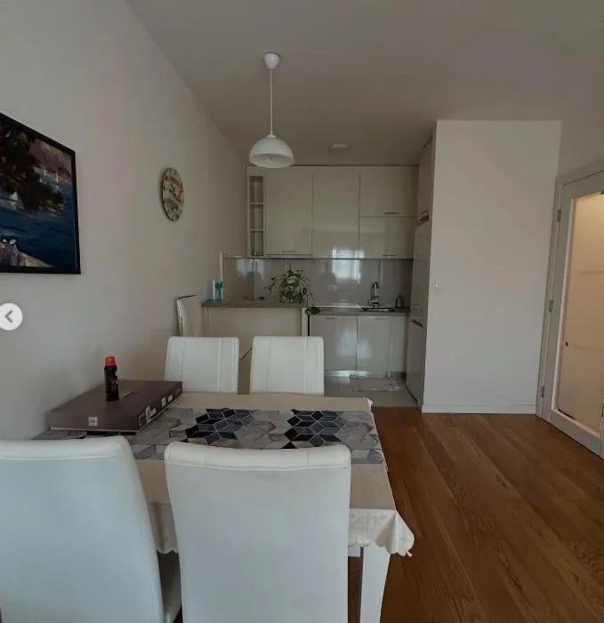 Dining area with a table and white chairs, overlooking a smaller kitchen in the background.