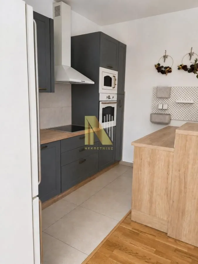 Moderna kuhinja sa tamnim elementima i ugrađenim uređajima.