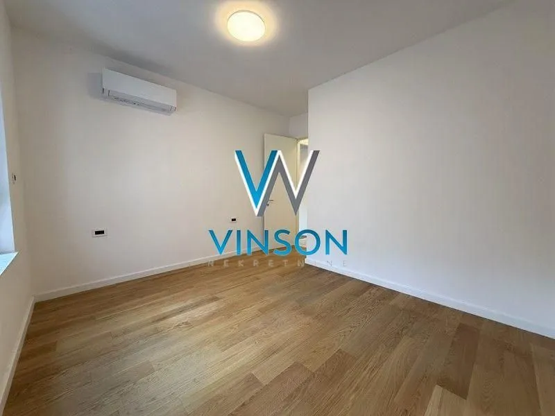 Empty room with white walls, wooden flooring, and an air conditioning unit.