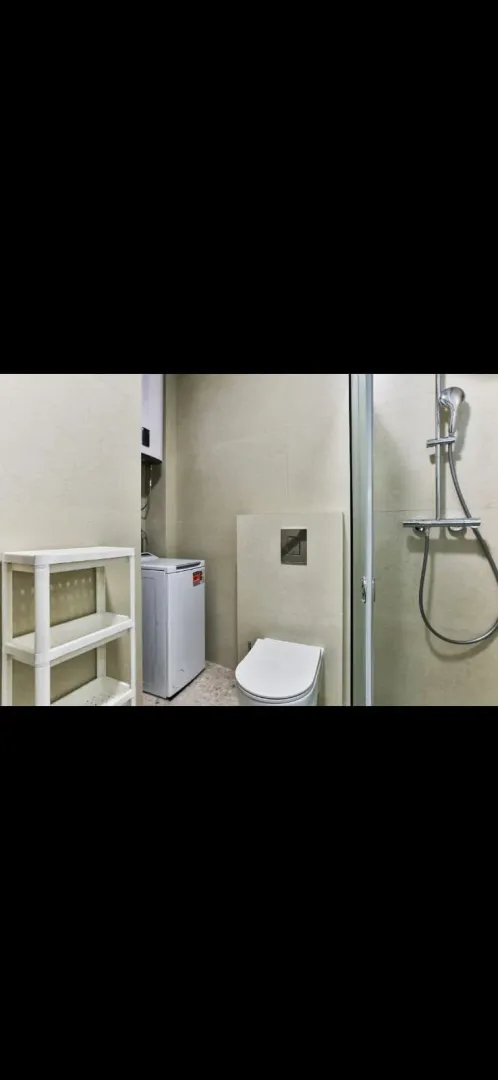 Manje kupatilo sa tuš kabinom, WC šoljom i veš mašinom.