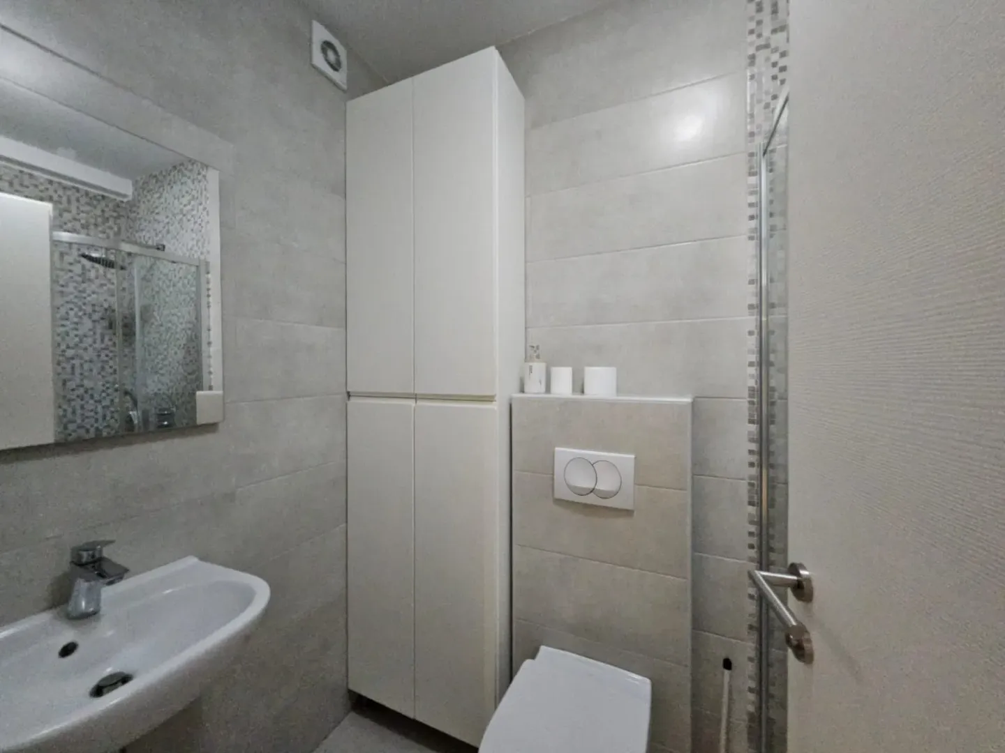 Modernly equipped bathroom with a sink, toilet, and white cabinet.