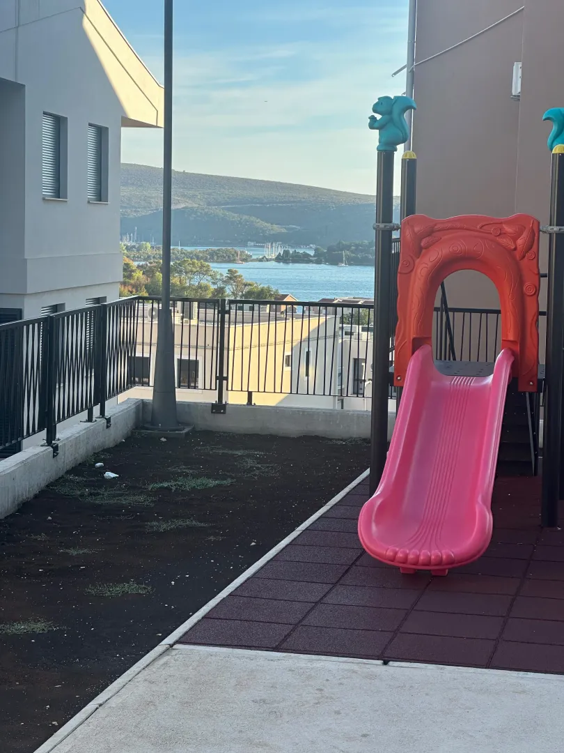 Dvorište zgrade sa dječijim igralištem i pogledom na more.