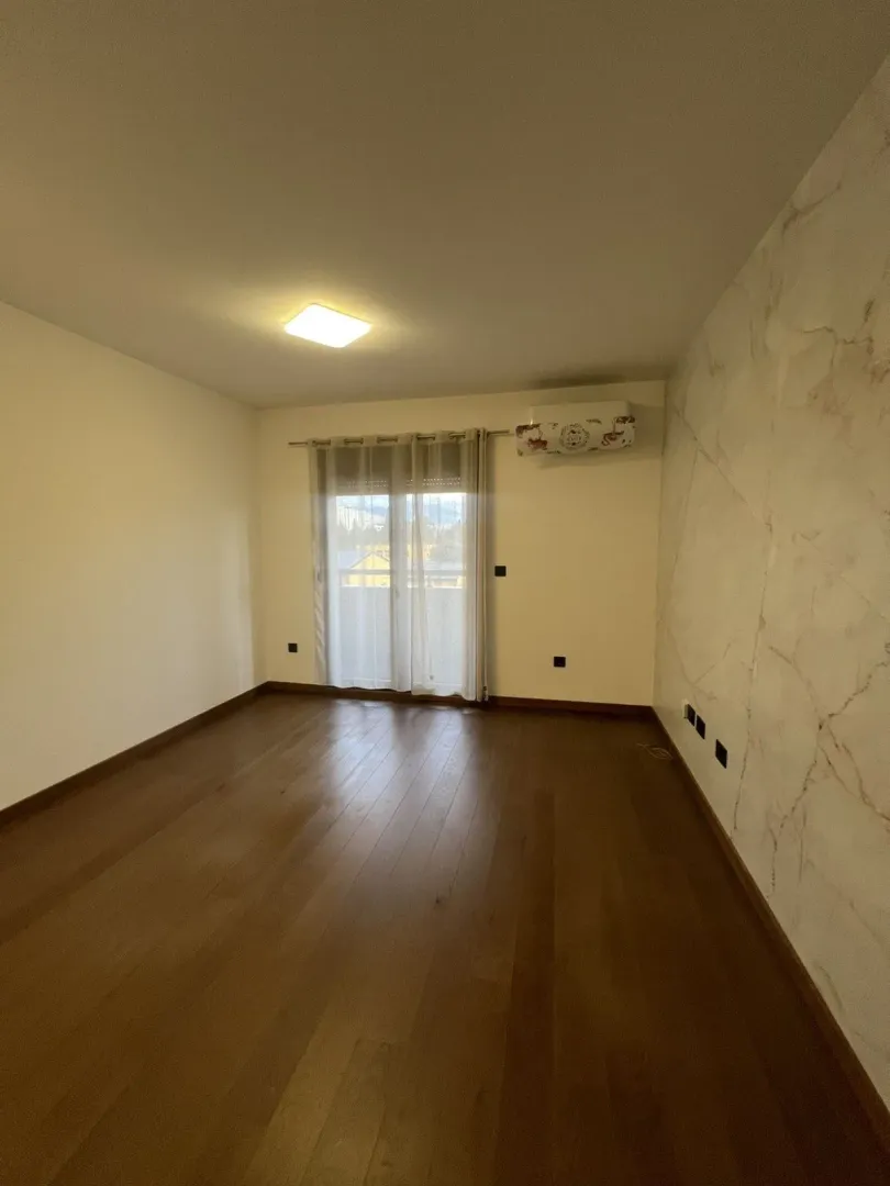 An empty room featuring wooden flooring, light walls, and a decorative marble-style accent wall.