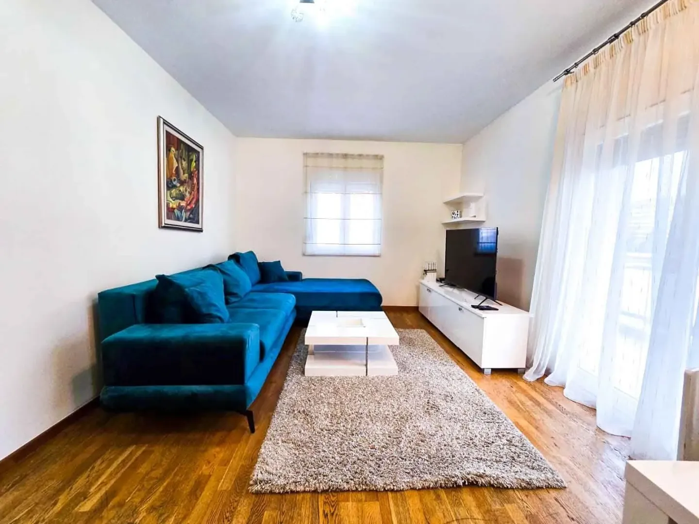 A bright living room with a blue sectional sofa, a white coffee table, and a television.