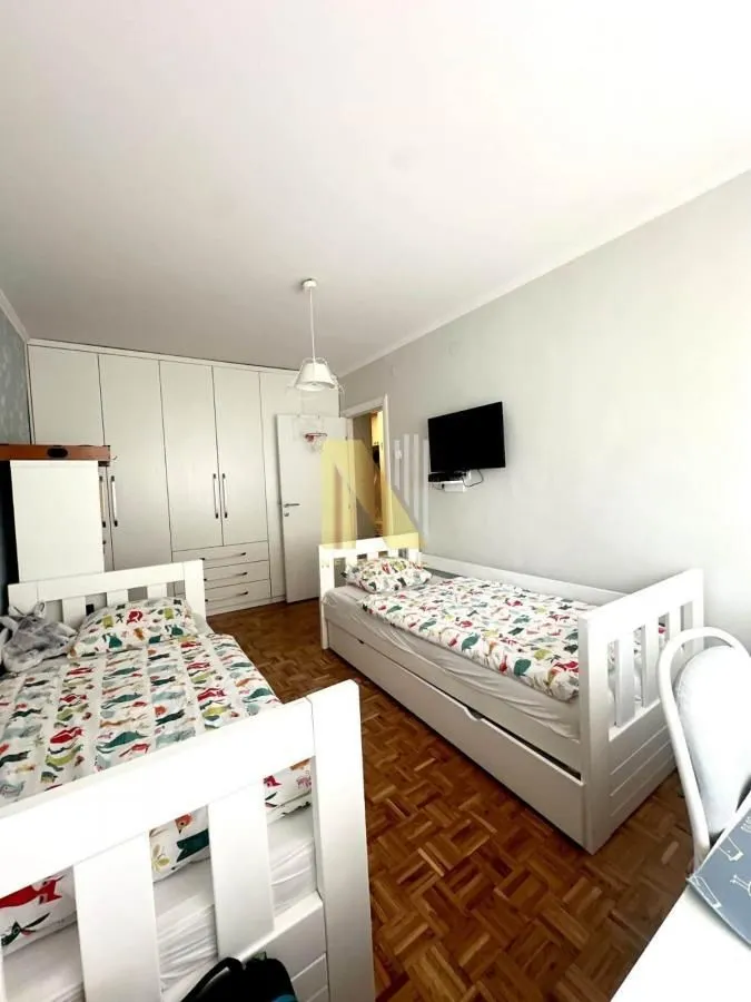 Dečja soba sa dva kreveta i belim garderoberom.
