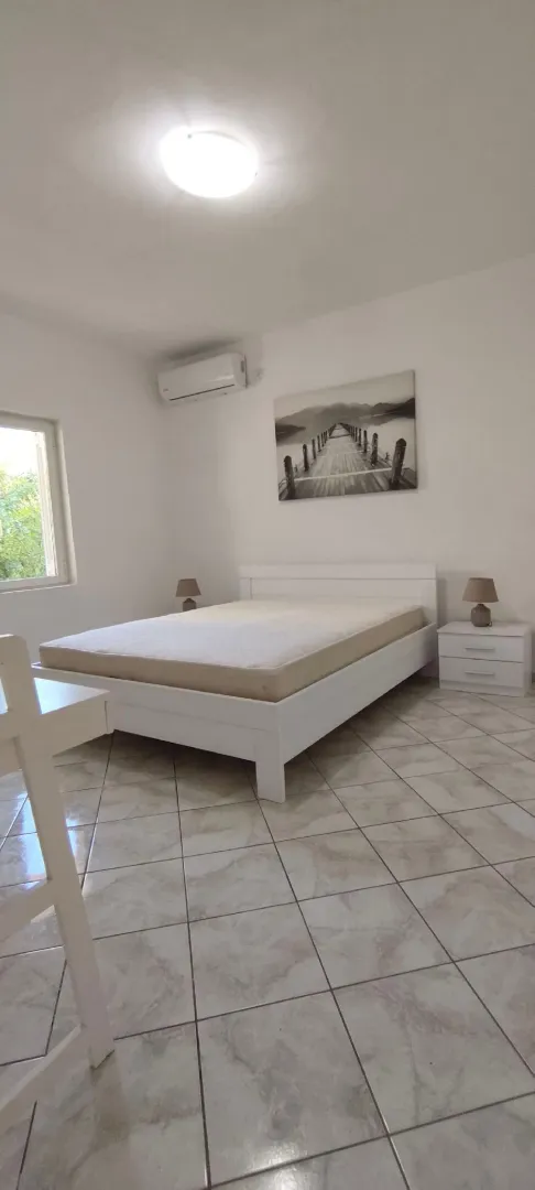 Bright bedroom with a white bed, nightstands, and an air conditioner.