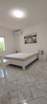 Bright bedroom with a white bed, nightstands, and an air conditioner. - image 2