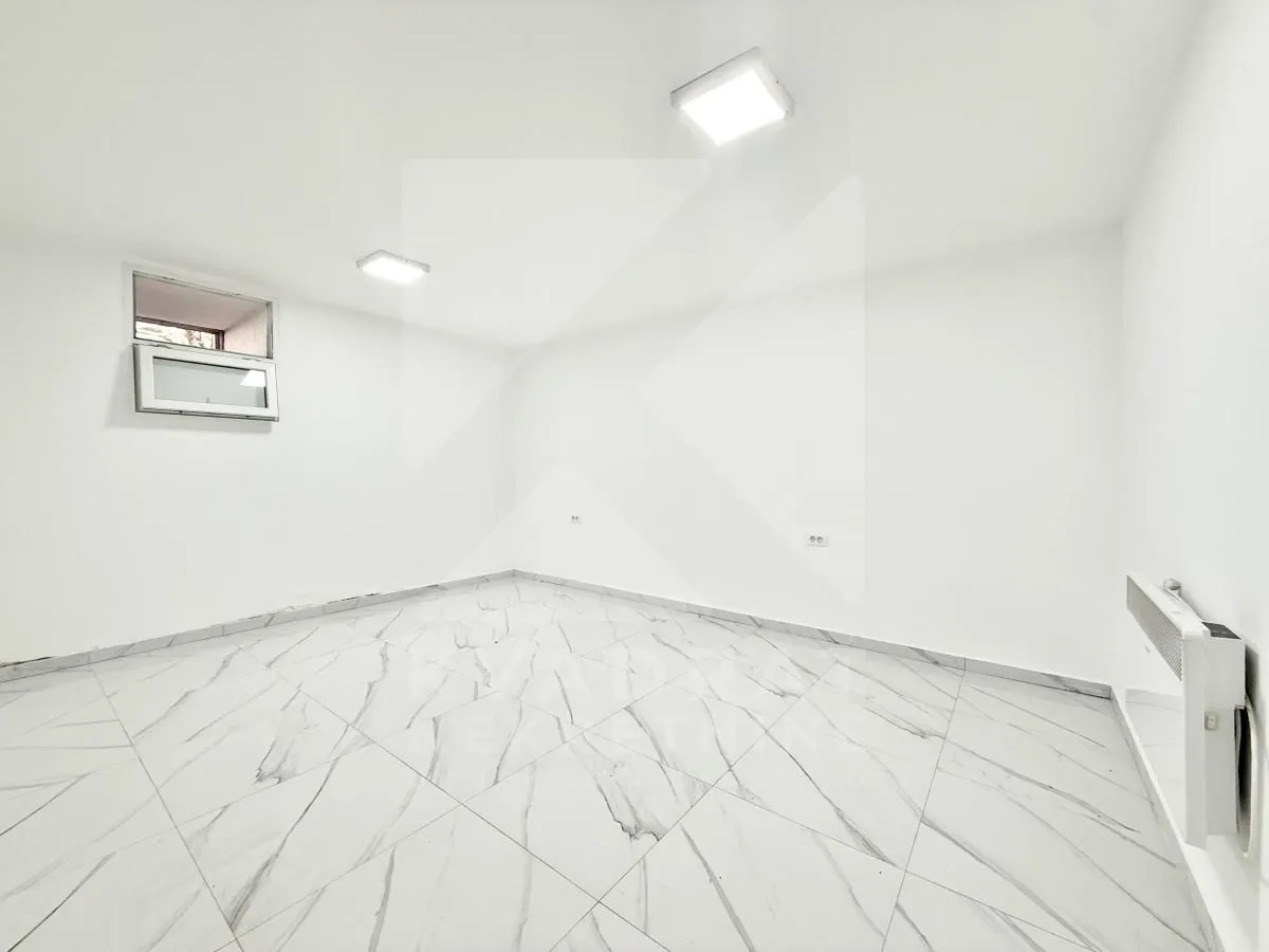 An empty room with white walls, marble floor tiles, and a small window.