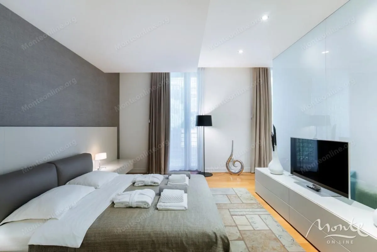 Moderna spavaća soba sa bračnim krevetom, televizorom i izlazom na terasu.