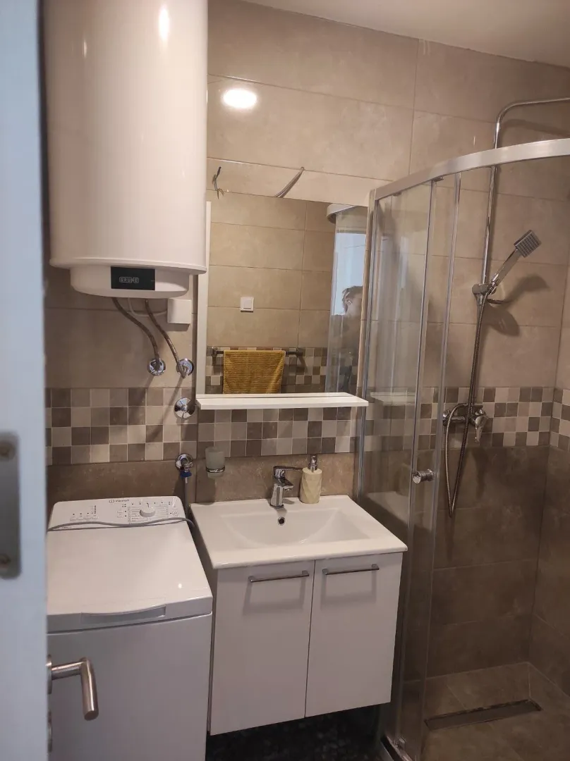 Smaller bathroom with a shower cabin, vanity, washing machine, and water heater.