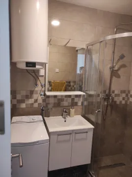 Smaller bathroom with a shower cabin, vanity, washing machine, and water heater. - image 4