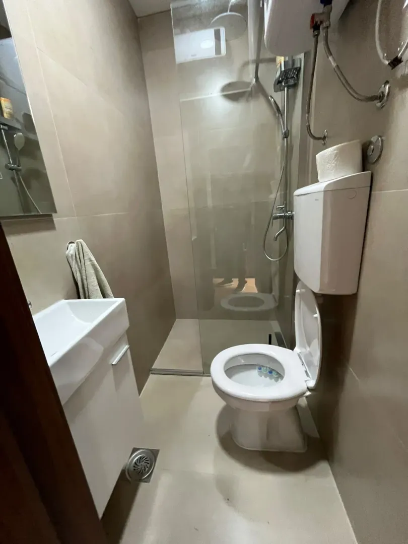Compact bathroom with a shower cabin, washbasin, and toilet in beige tones.