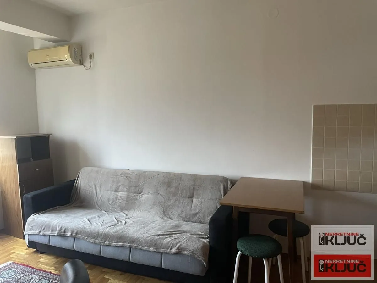 Dnevna soba sa kaučem, trpezarijskim stolom i klima uređajem na zidu.