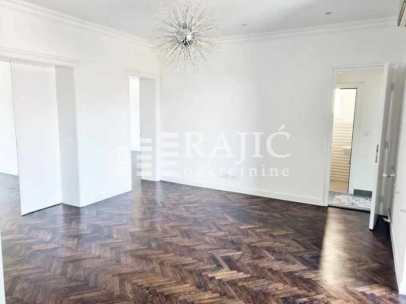 Bright empty room with parquet flooring and a decorative chandelier.