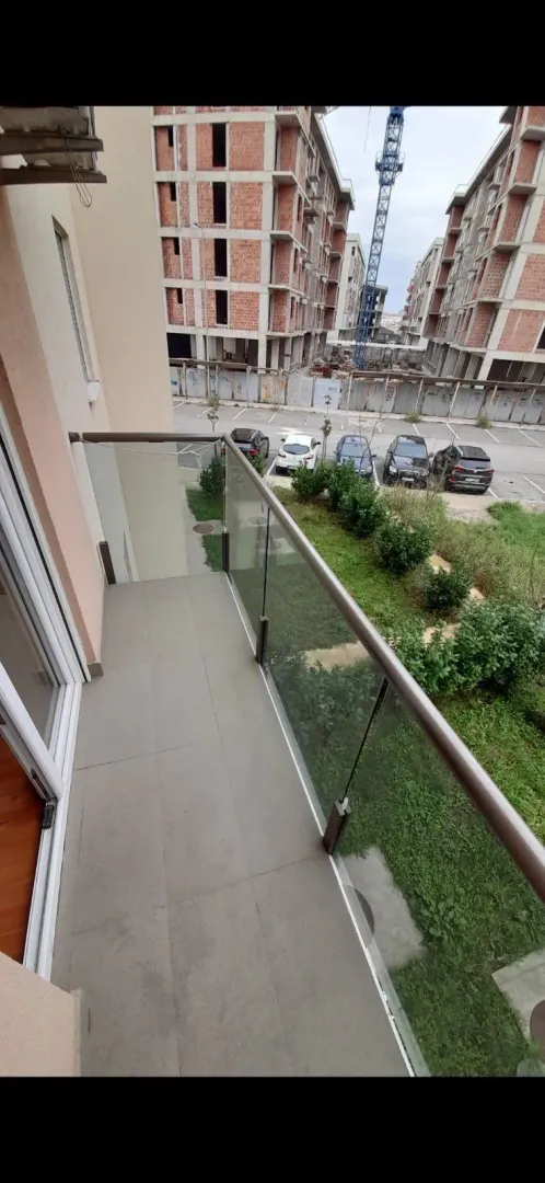 Balkon sa staklenom ogradom i pogledom na parking.