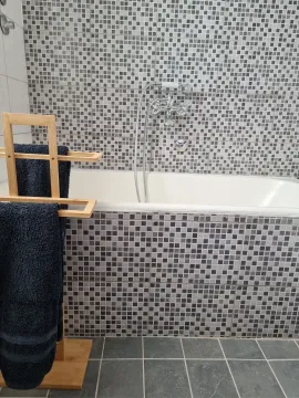 Bathroom with a bathtub tiled in mosaic tiles and a wooden towel rack. - image 12