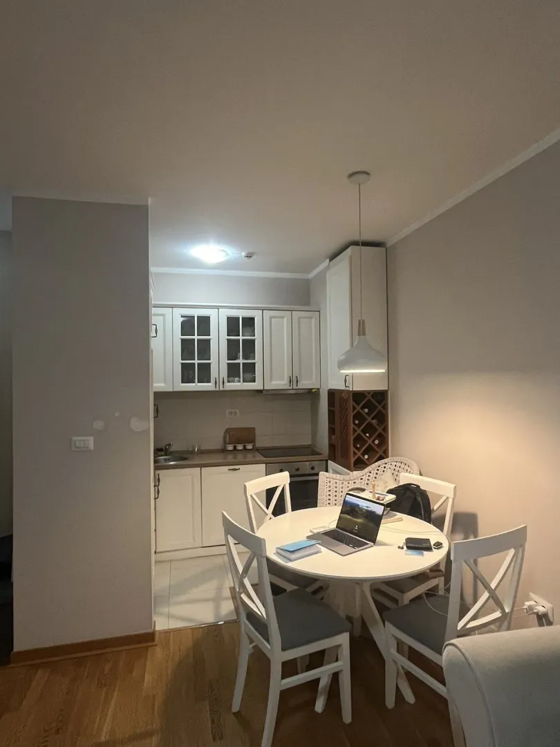 Bright dining area with a round table and a small kitchen in the background.