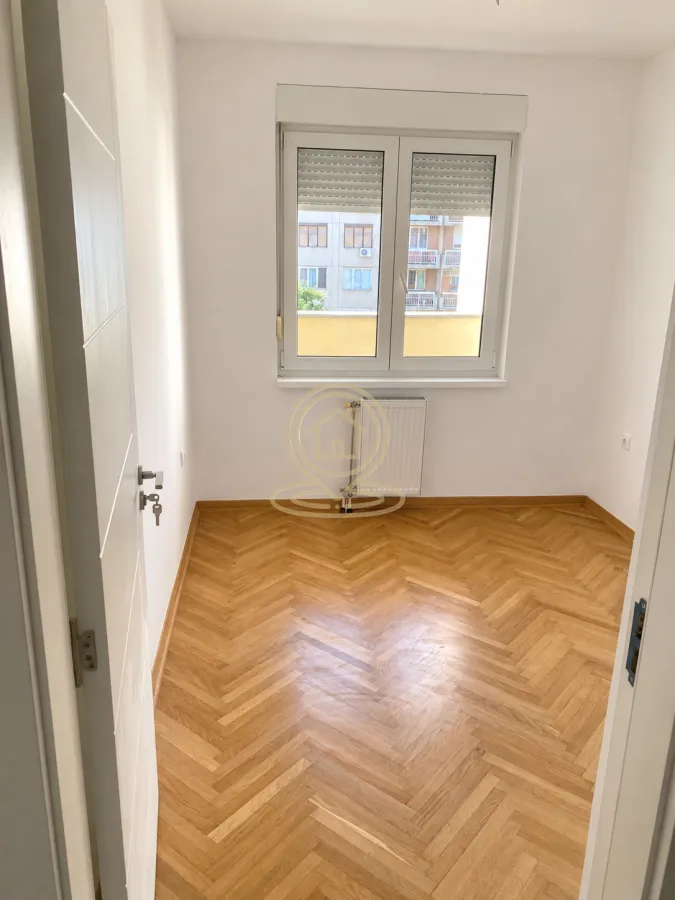 Prazna soba sa drvenim parketom i prozorom.