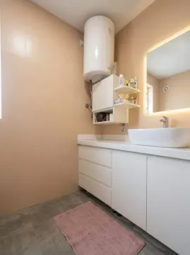 Modern bathroom with a white sink, cabinet, and water heater. - image 11
