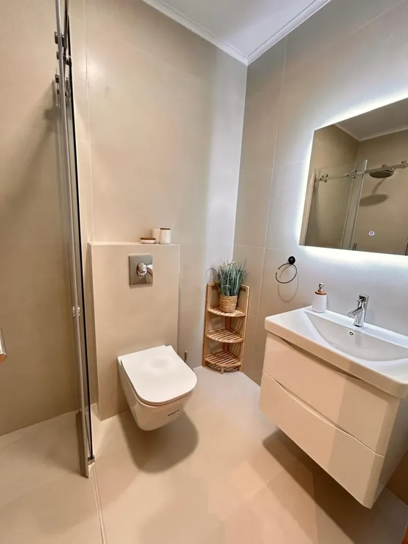 Modern bathroom with light tiles, a sink, and a toilet.