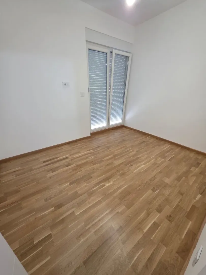 Prazna soba sa parketom i balkonskim vratima.