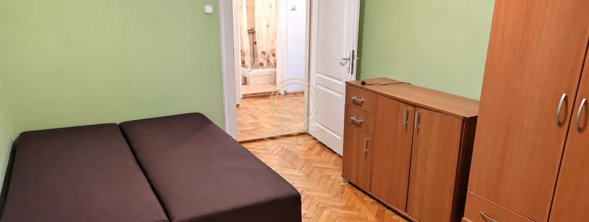 Nameštena spavaća soba sa bračnim krevetom, ormarom i drvenim podom.