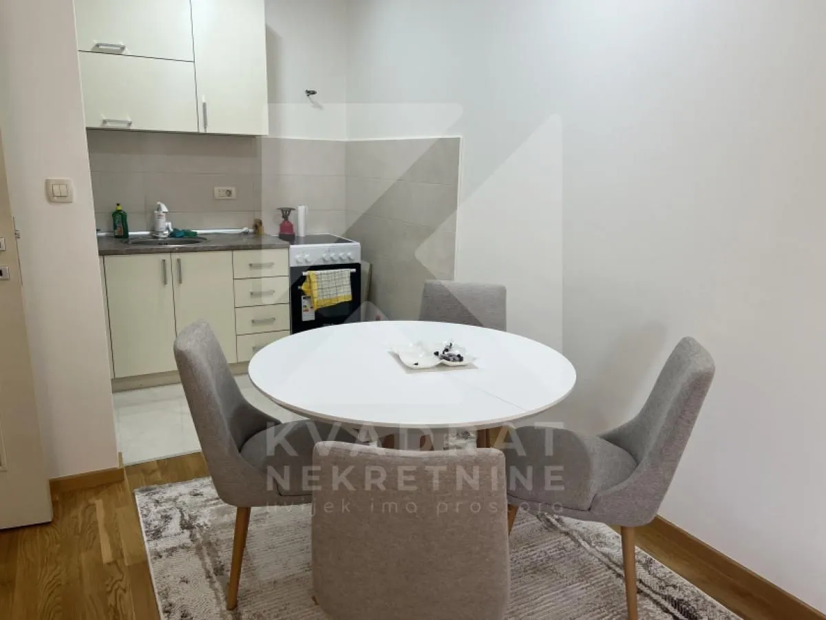 Dining table with four chairs and a small kitchen in the background.