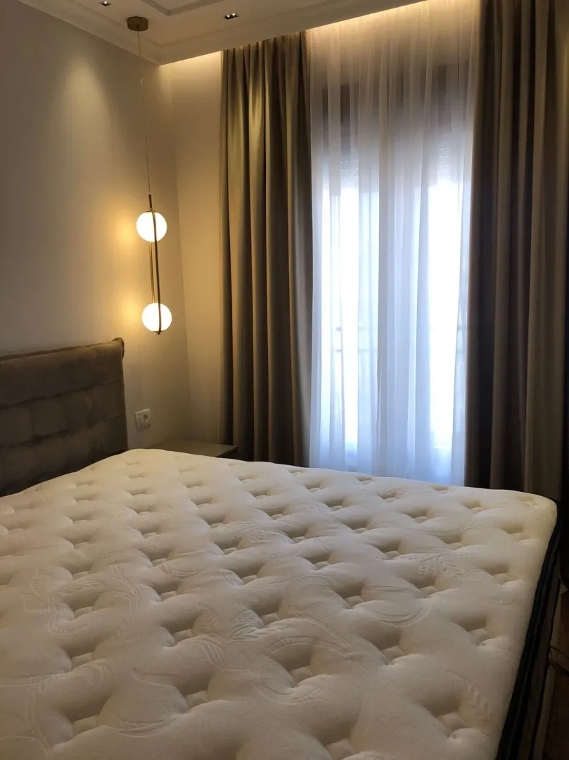 A bedroom with a large bed, modern lighting, and curtains on the window.