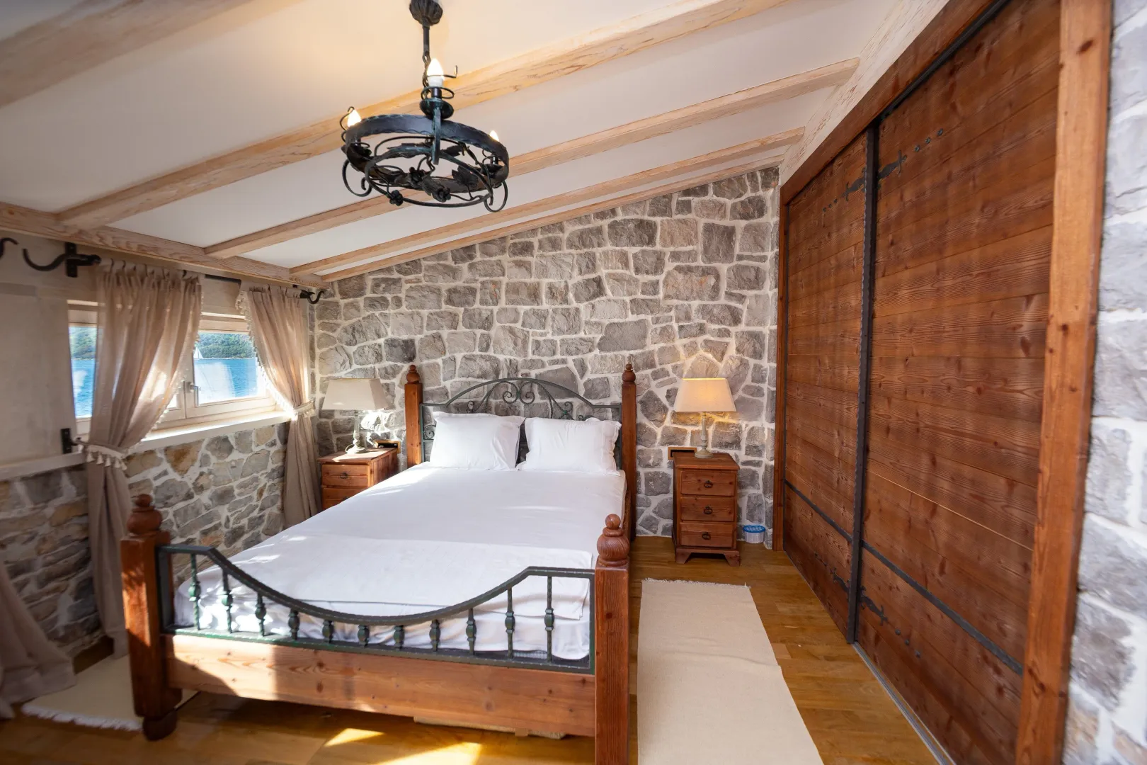 Bedroom with a double bed, stone wall, and wooden beamed ceiling.