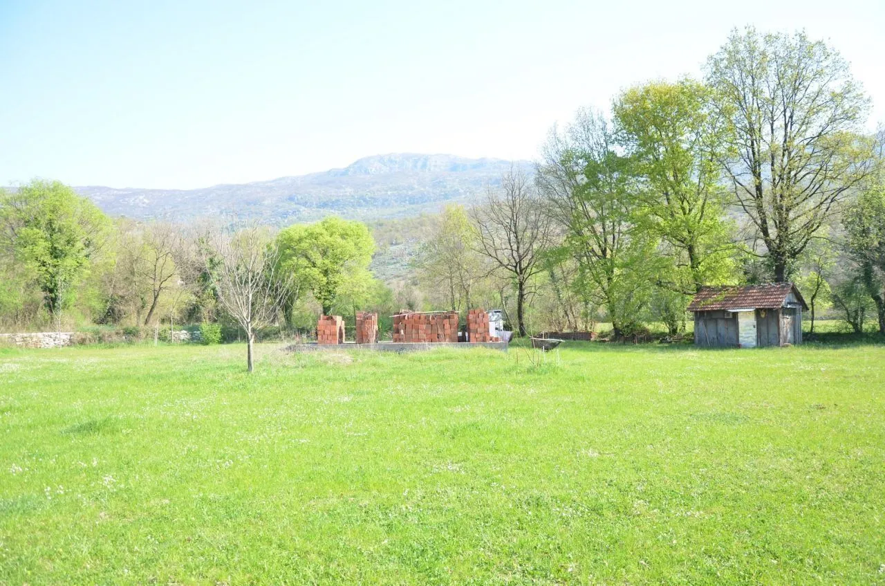Prostran zeleni plac sa građevinskim materijalom i malom pomoćnom kućicom.